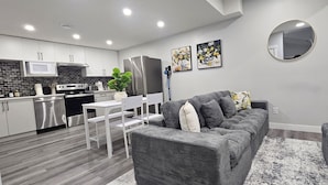 A modern kitchen with stainless steel appliances and a dining area with a gray sofa and white table.