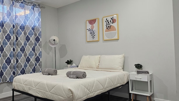 A bedroom with a bed, a bedside table, a floor lamp, and two wall art pieces.