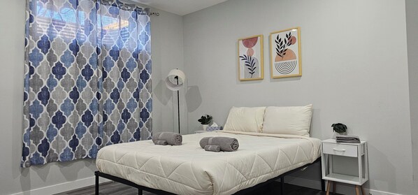 A bedroom with a bed, a bedside table, a floor lamp, and two wall art pieces.