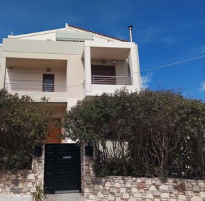 Un edificio de dos pisos con fachada de piedra, una reja negra y un cielo azul despejado.