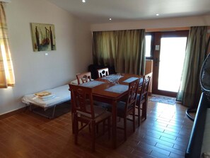 A dining area with a wooden table and chairs, a bench with a folded blanket, and a painting on the wall. - Sofita Di Sofo Kos Vacation Apartment (Kos)