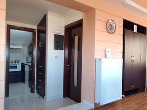 A hallway leading to a kitchen with a microwave, oven, and cabinets. There is a door with a light switch and a thermostat on the wall. - Sofita Di Sofo Kos Vacation Apartment (Kos)