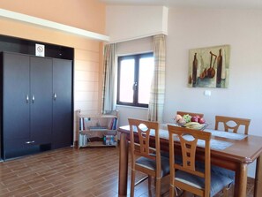 Un comedor con mesa y sillas de madera, una estantería y un ventanal con cortinas.