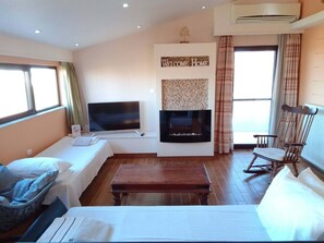 Una sala de estar con televisor de pantalla plana, chimenea, sofá, banco de madera y mecedora.