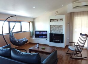 A modern living room with a hanging chair, a sofa, a television, and a fireplace. - Sofita Di Sofo Kos Vacation Apartment (Kos)