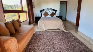 A bedroom with a bed, a sofa, a window with a view, and a door.