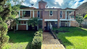 A two-story house with a brick exterior, a small tower-like structure on the roof, and a well-maintained lawn.
