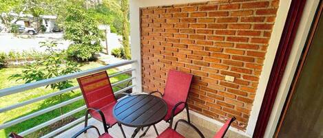A balcony with a brick wall, a round table, and four red chairs.