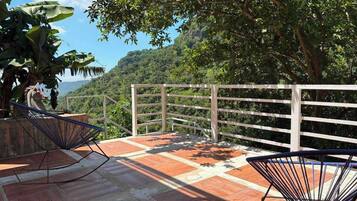 Una terraza con vistas a un paisaje montañoso, que incluye una barandilla de madera y dos sillas.