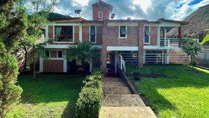 Una casa de dos pisos con fachada de ladrillo, una estructura tipo torre en el techo y un césped bien cuidado.