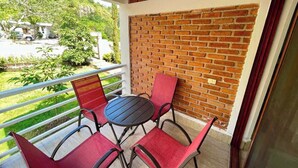 Un balcón con un muro de ladrillo, una mesa redonda y cuatro sillas rojas.