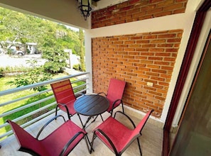 Ein Balkon mit einer Ziegelwand, einem runden Tisch und vier roten Stühlen.