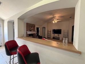 Eine moderne Küche mit Kamin aus Ziegelsteinen, einer Bar mit zwei roten Stühlen und einem Deckenventilator.