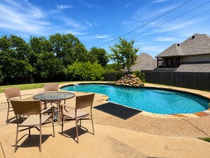 Ein Garten mit Pool, einer Terrasse mit Stühlen und einem Haus im Hintergrund.