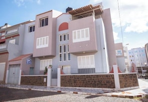 A multi-story residential building with balconies, a stone wall, and a gated entrance. - Enjoyable 1-bedroom apartment in adorable Mindelo neighborhood (Mindelo)