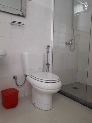 A bathroom with a toilet, a shower, and a red trash bin. - Enjoyable 1-bedroom apartment in adorable Mindelo neighborhood (Mindelo)