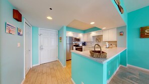 Une cuisine moderne avec des armoires blanches, des appareils en acier inoxydable et un mur d’accent de couleur turquoise.