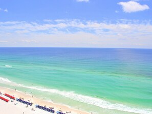 Een strand met helder turquoise water, een zandstrand en een rij strandparasols.