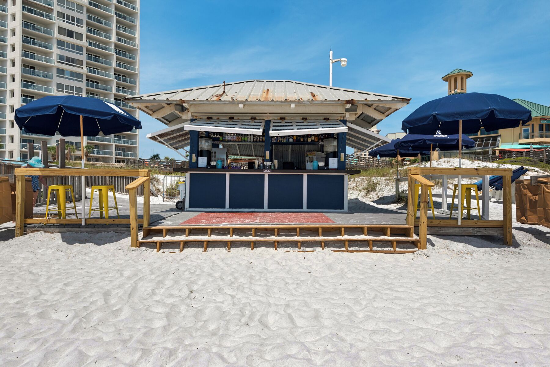A beachside kiosk with a metal roof and a wooden bench area.