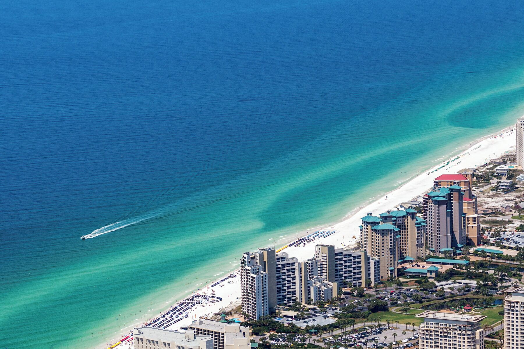 A coastal cityscape with high-rise buildings, a beach, and a clear blue sea.