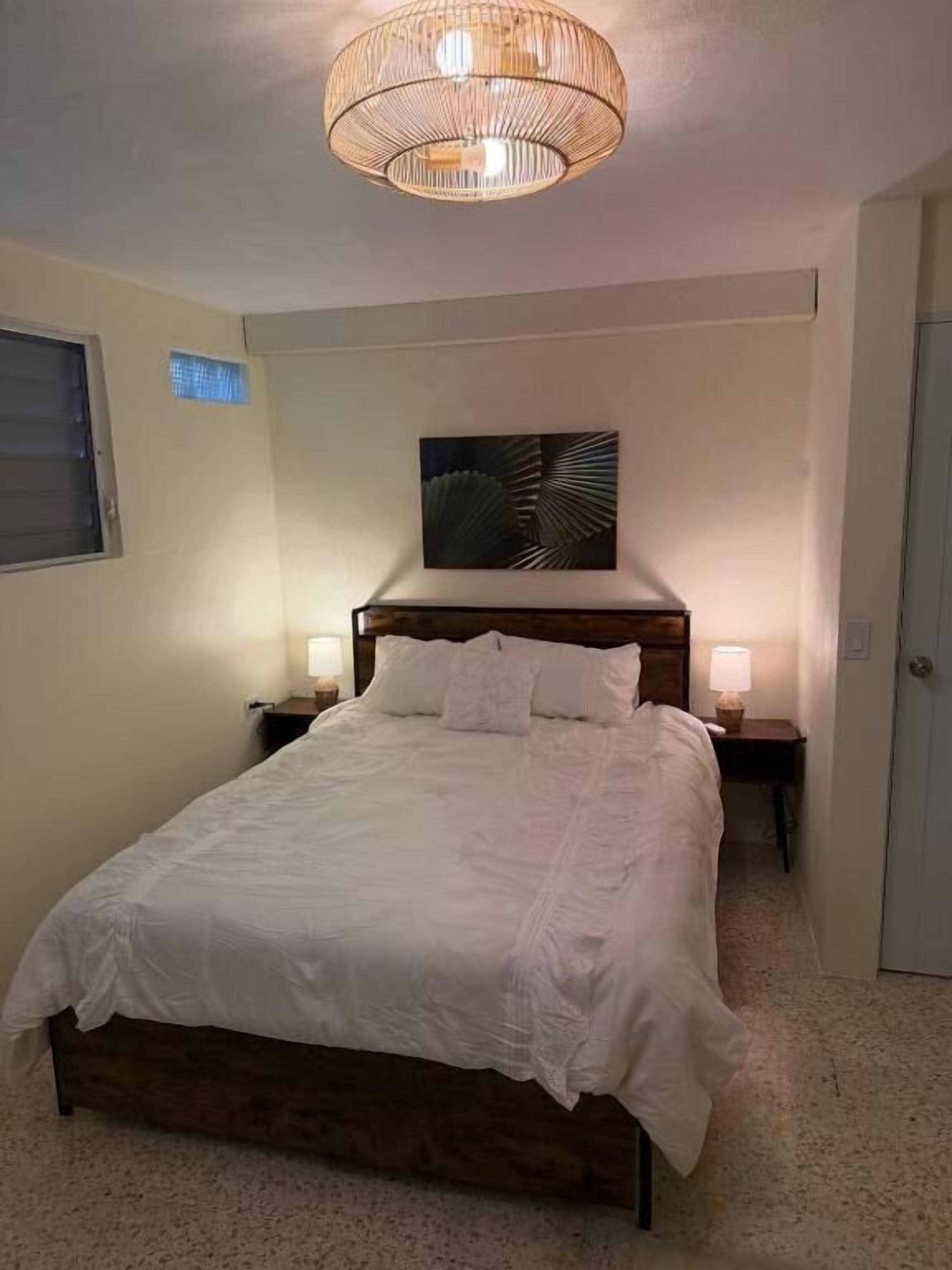 A bedroom with a large bed, bedside lamps, a ceiling light fixture, and a wall-mounted artwork.
