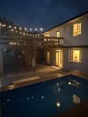 A two-story building with a swimming pool, outdoor lighting, and a covered area.