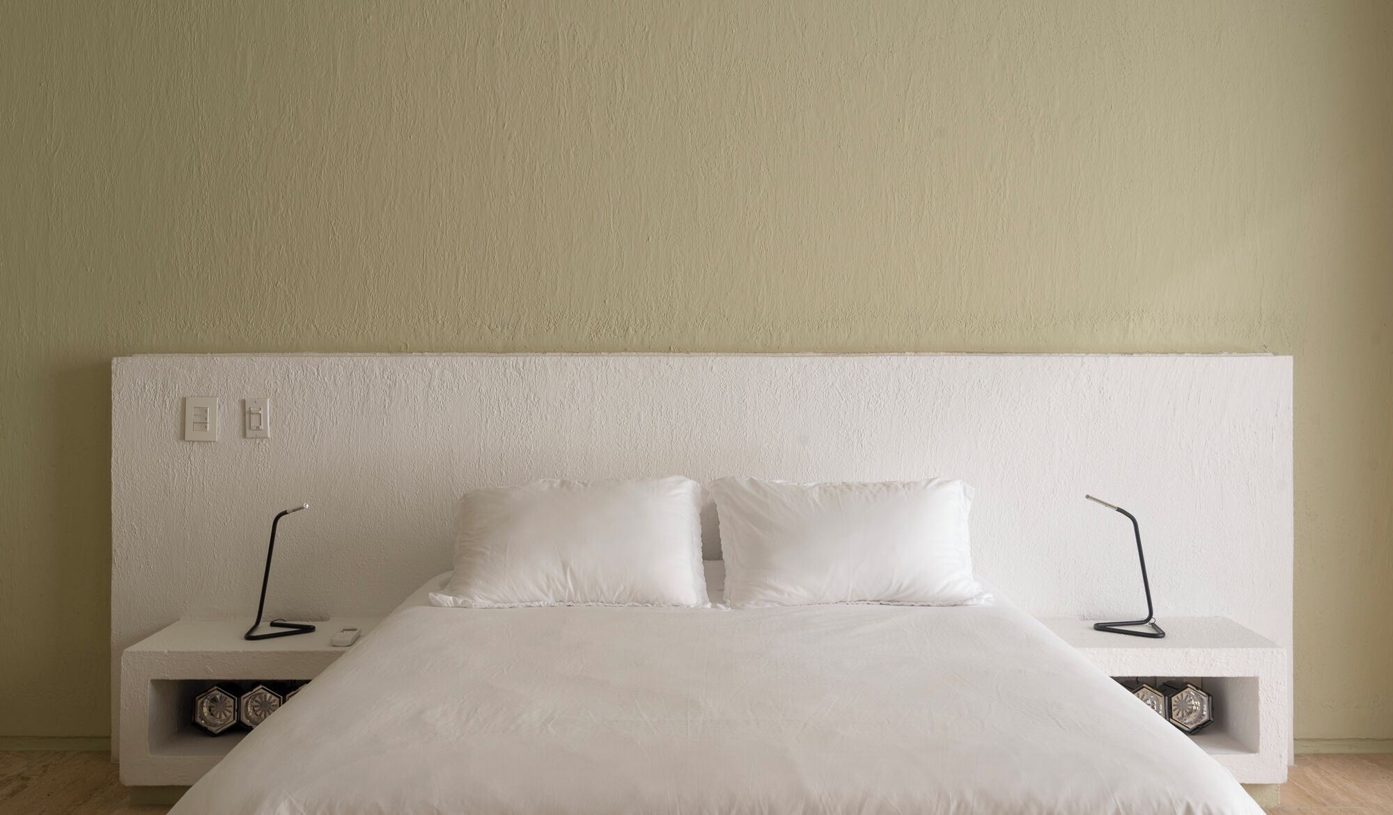 Ein schlichter Schlafzimmerbereich mit einem großen Bett, zwei Nachttischen und einer schlichten Wand.