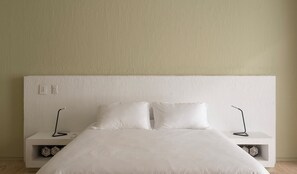 Ein schlichter Schlafzimmerbereich mit einem großen Bett, zwei Nachttischen und einer schlichten Wand.