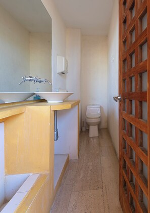 A bathroom with a sink, mirror, toilet, and a wooden door. - Luxury Loft Parque de Novios-ByHuespedia (Santa Marta)