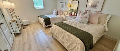 Une chambre avec deux lits, un ventilateur de plafond, une fenêtre avec des stores et une table de chevet avec une lampe.