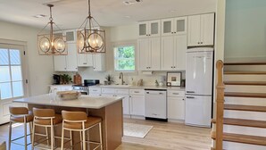 Una cocina moderna con armarios blancos, una isla central con taburetes e iluminación colgante.