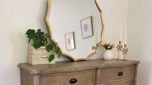 Un aparador de madera con un espejo de marco dorado, cajones y un jarrón con flores.