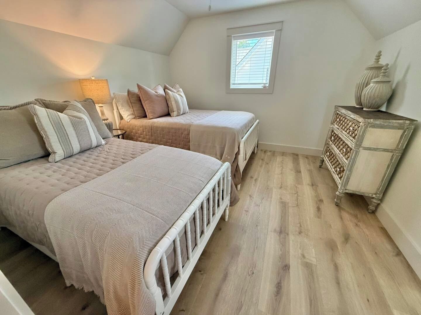 A bedroom with two beds, a nightstand, a dresser, and a window.