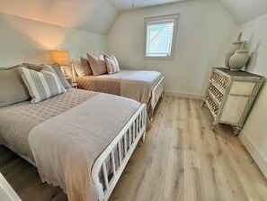 Un dormitorio con dos camas, una mesita de noche, un aparador y una ventana.