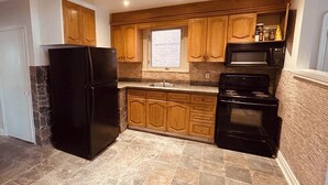 A compact kitchen with wooden cabinets, a black refrigerator, a microwave, and a stove.