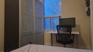 A bedroom with a bed, a desk with a chair, a window, and a wardrobe.