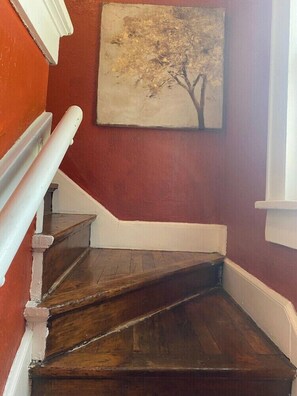 A wooden staircase with white trim against a red wall, leading to a landing with a framed picture. - Cozy Retreat in Fort Worth (Fort Worth)
