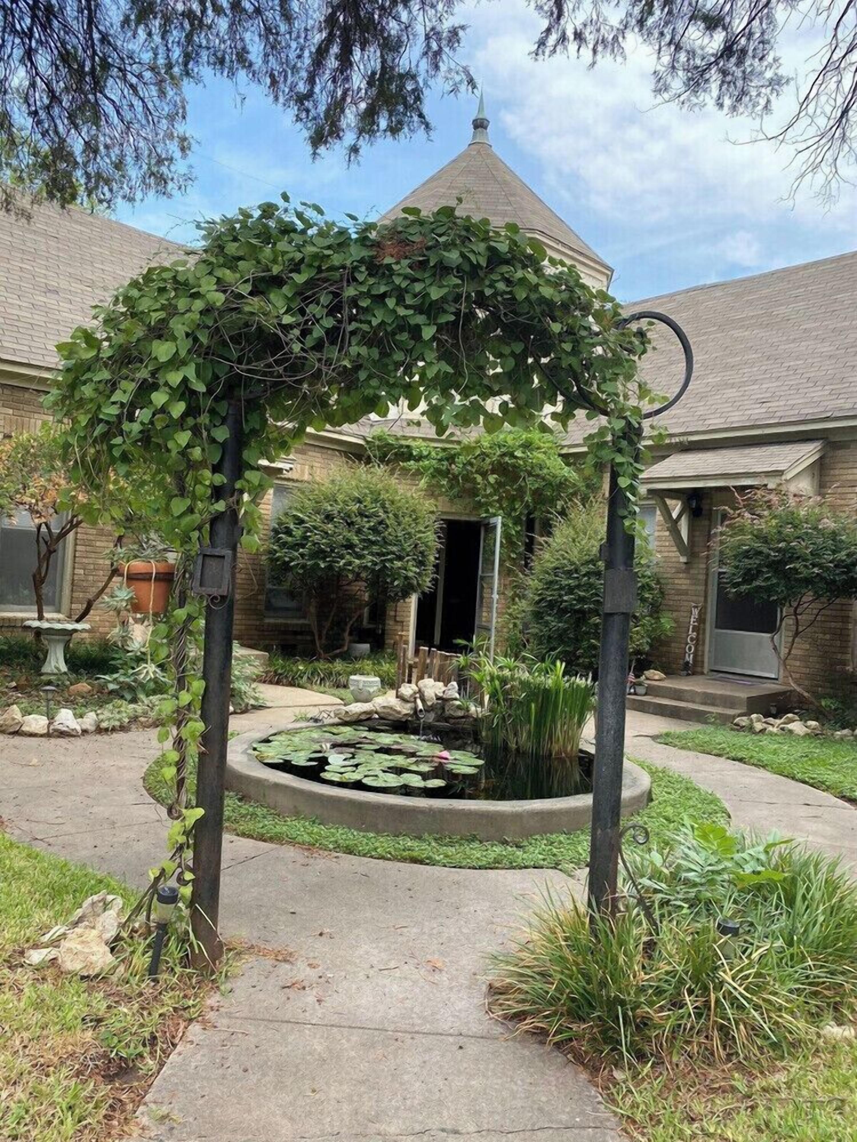 A garden with a circular pond, a pergola, and a brick building with a conical roof.