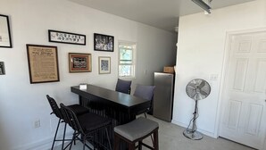 Een eethoek met een tafel en stoelen, een ventilator en ingelijste foto's aan de muur.