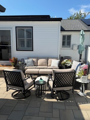 A patio with a beige sofa, two chairs, a small table, and a potted plant. - Perfect 2-bedroom cottage in the Village Green Community of enchanting Cape May (Cape May)