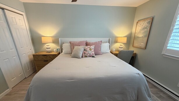 Een slaapkamer met een groot bed, twee nachtkastjes met lampen, een plafondventilator, een deur en een lijst met een afbeelding aan de muur.