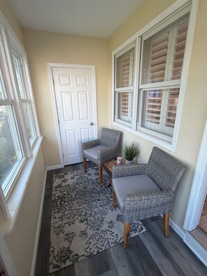 A corner room with a door, two wicker chairs, a small table, a potted plant, and a patterned rug. - Perfect 2-bedroom cottage in the Village Green Community of enchanting Cape May (Cape May)