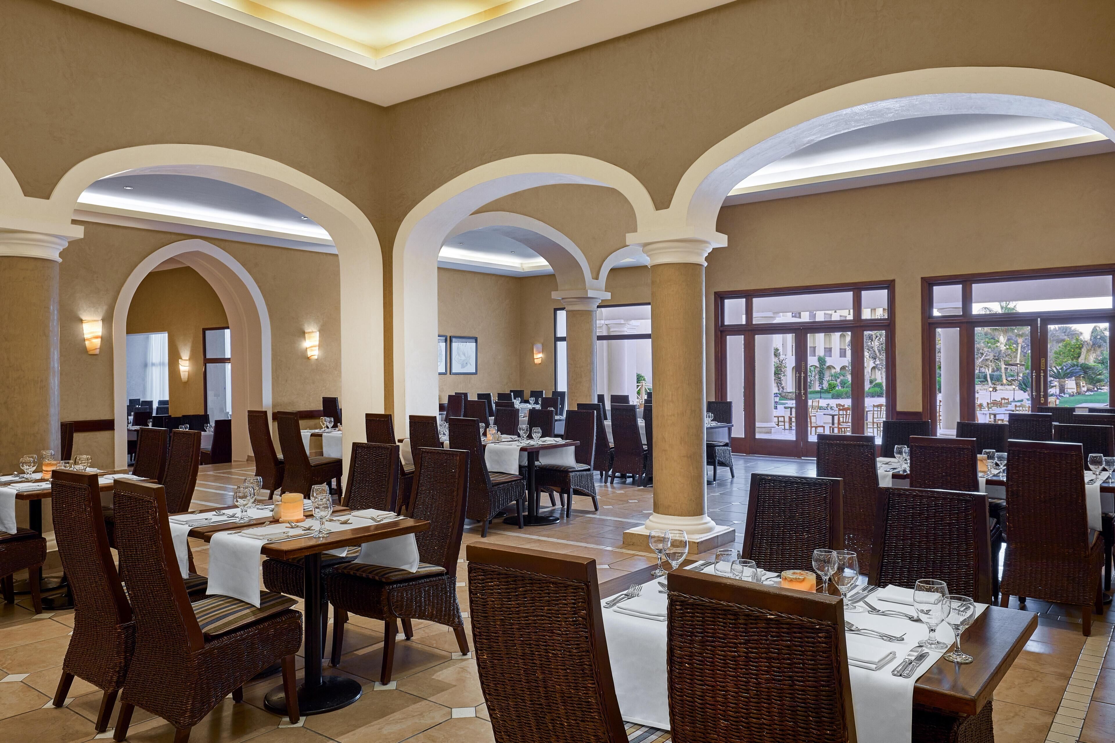 Un'ampia sala da pranzo con diversi tavoli e sedie, ampie finestre e un soffitto alto con colonne ad arco.