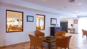 A dining area with wicker chairs, a wooden table, and a large mirror reflecting the room. - Rocaplana Hostal (Formentera)