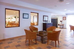 A dining area with wicker chairs, a wooden table, and a large mirror reflecting the room. - Rocaplana Hostal (Formentera)