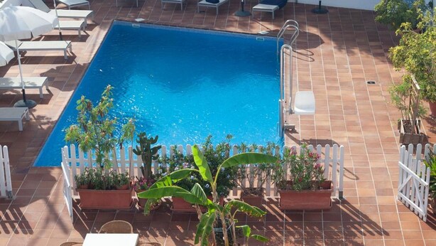 A swimming pool with lounge chairs and tables, surrounded by potted plants and a white picket fence. - Rocaplana Hostal (Formentera)