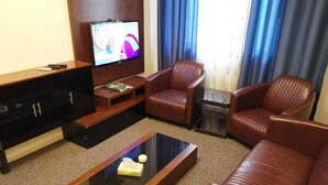 Une chambre d’hôtel équipée d’un téléviseur à écran plat, de canapés en cuir, d’une table basse et d’un meuble de rangement en bois pour les appareils multimédias.