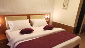 Une chambre d’hôtel comprenant un lit, deux tables de chevet, une petite table, une lampe fixée au mur et un tableau encadré accroché au mur.