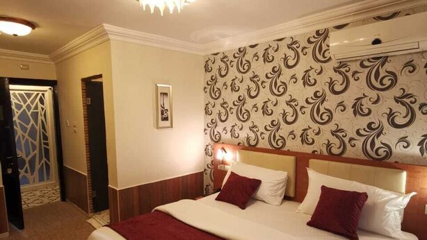 Une chambre d’hôtel avec un grand lit, un lustre, un papier peint à motifs et une porte ornée d’un motif géométrique.