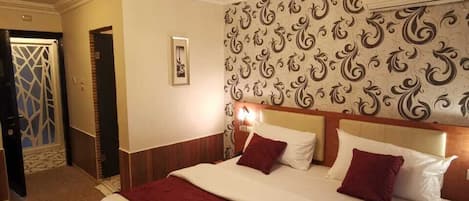Une chambre d’hôtel avec un grand lit, un lustre, un papier peint à motifs et une porte ornée d’un motif géométrique.